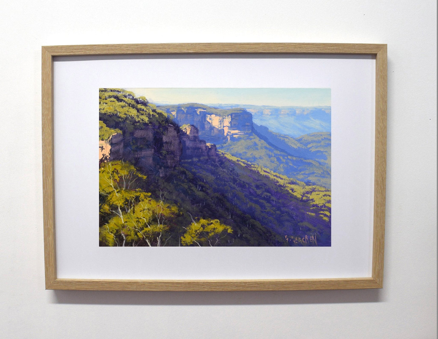 Framed painting of a mountain landscape with trees on a white wall