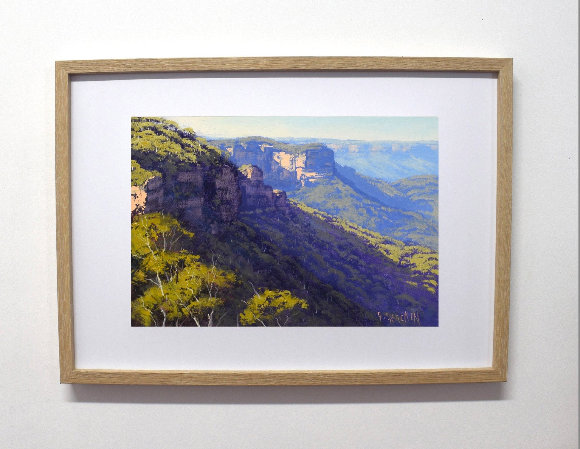 Framed painting of a mountain landscape with trees on a white wall