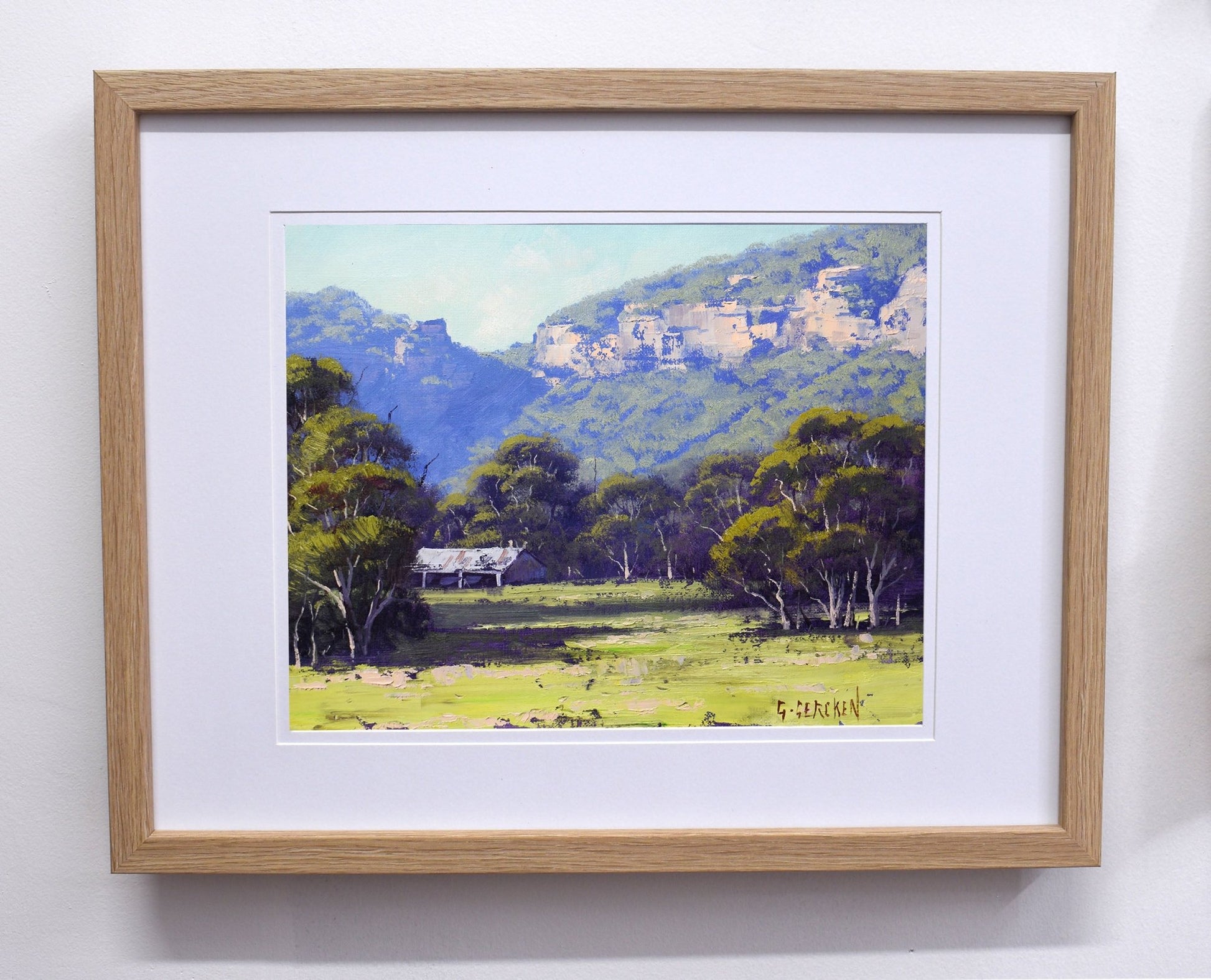 Framed painting of a landscape with mountains and trees on a white wall