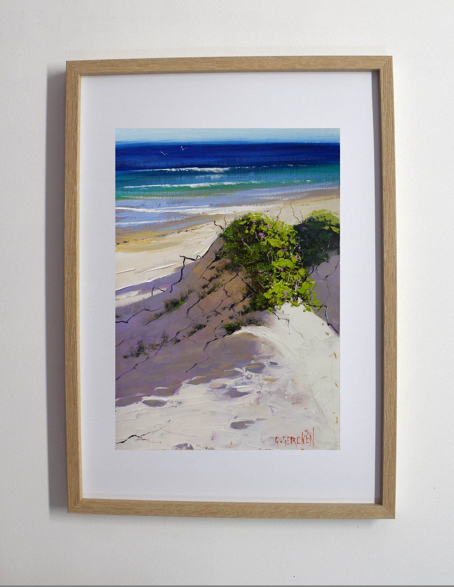 Framed painting of a beach scene with a tree on a white wall