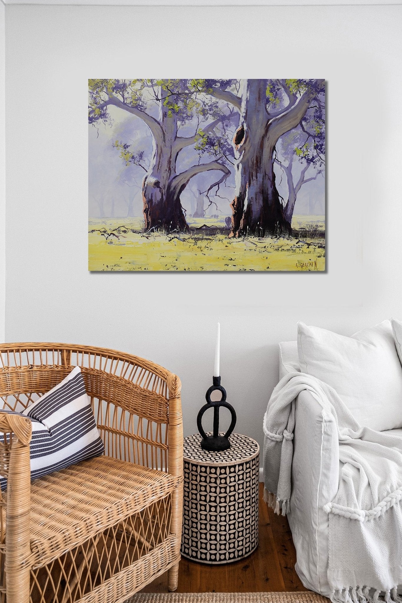 Room interior with a wicker chair, white sofa, and wall art of trees.