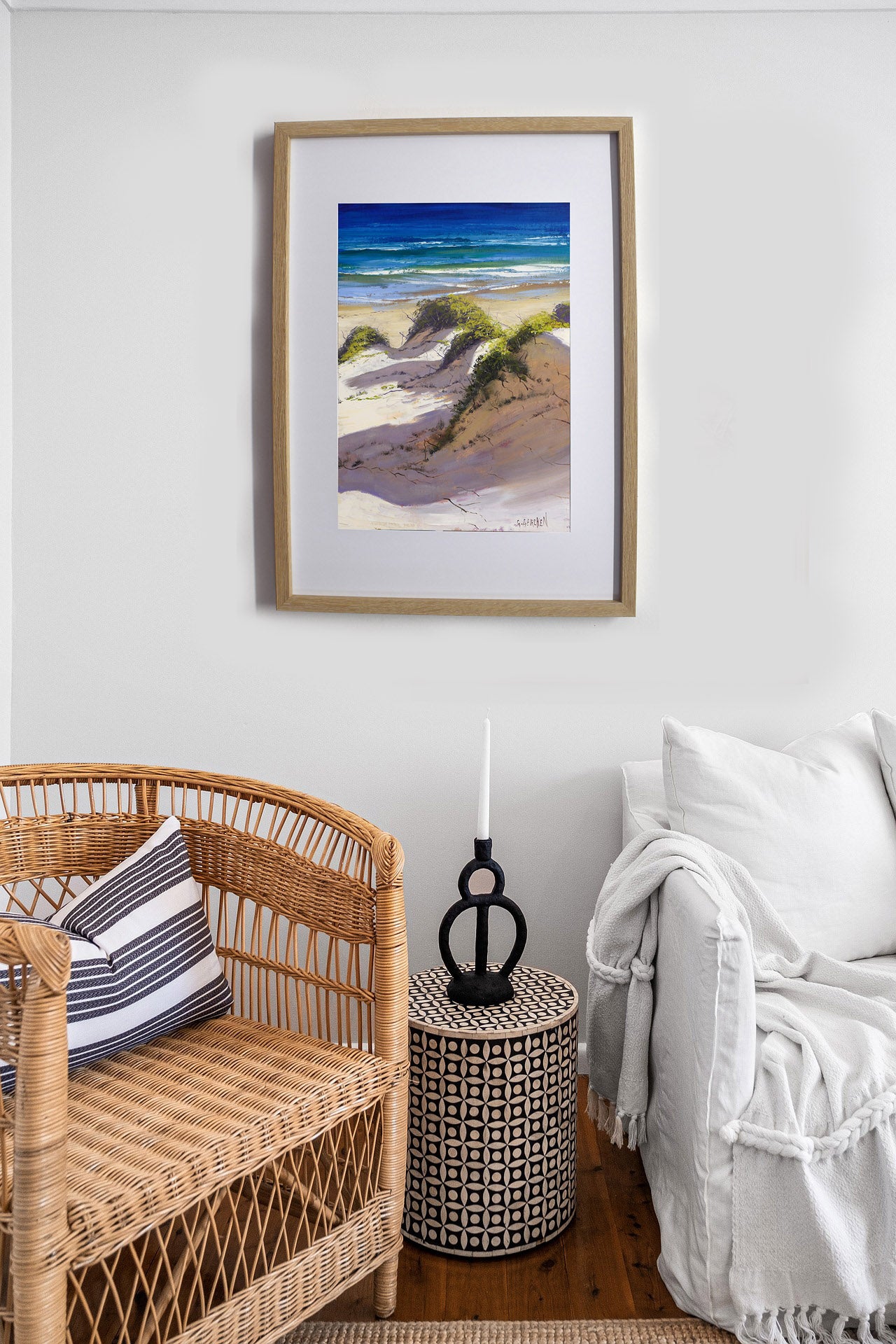 Living room with wicker chair, white sofa, and framed beach scene artwork on wall.