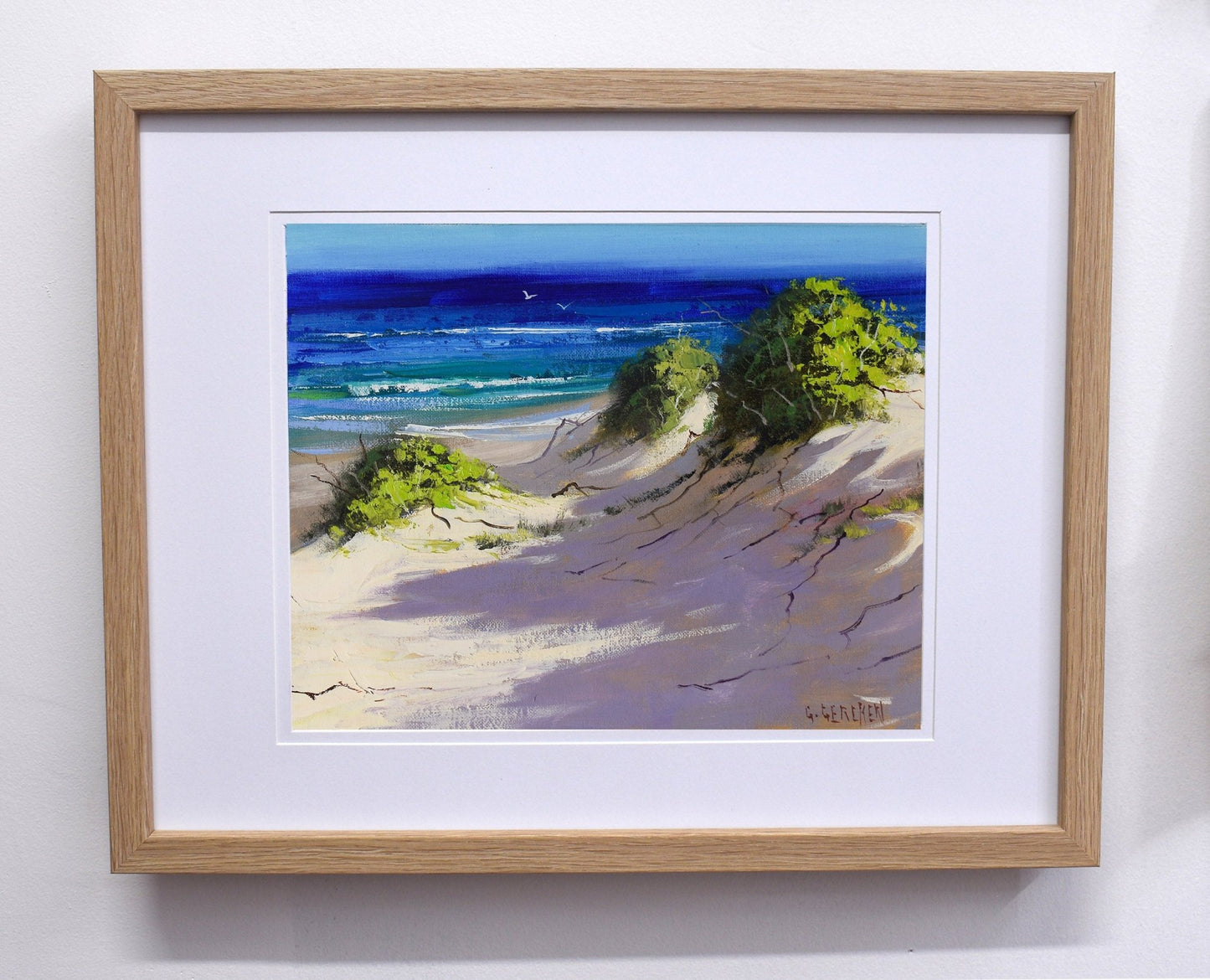 Framed painting of a beach scene with trees and ocean.