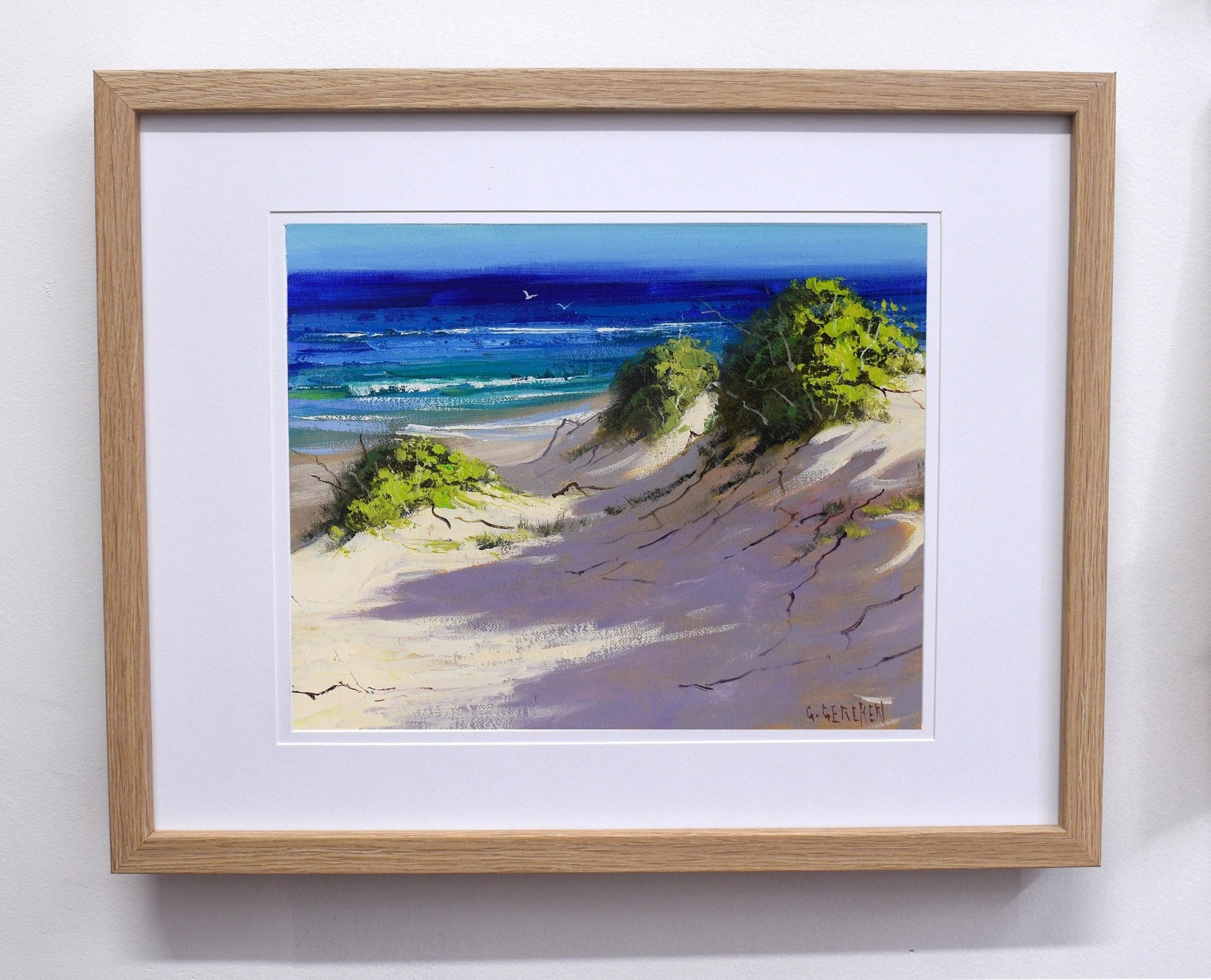 Framed painting of a beach scene with trees and ocean.