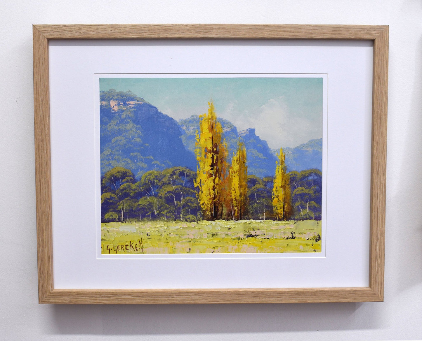 Framed painting of a landscape with yellow trees and mountains.