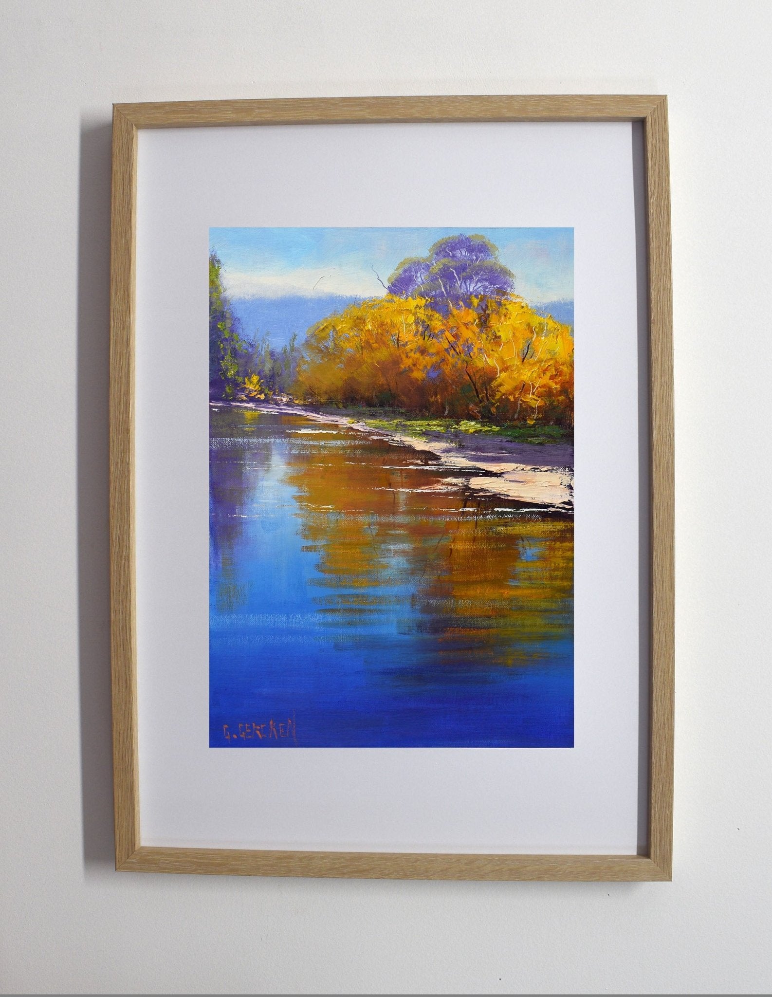 Framed painting of a landscape with trees and water on a white wall