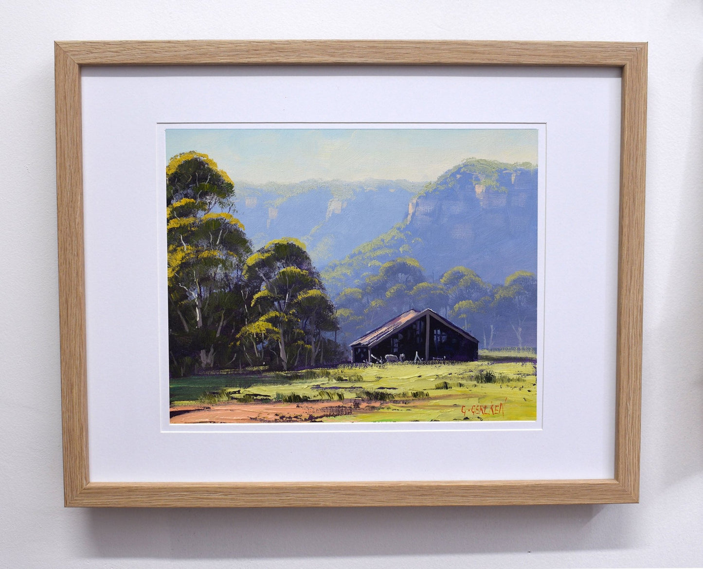 Framed painting of a landscape with trees and a building.