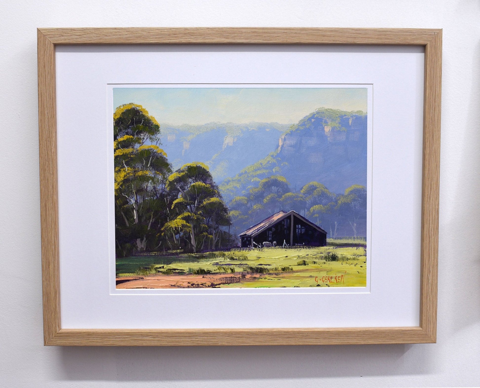 Framed painting of a landscape with trees and a building.